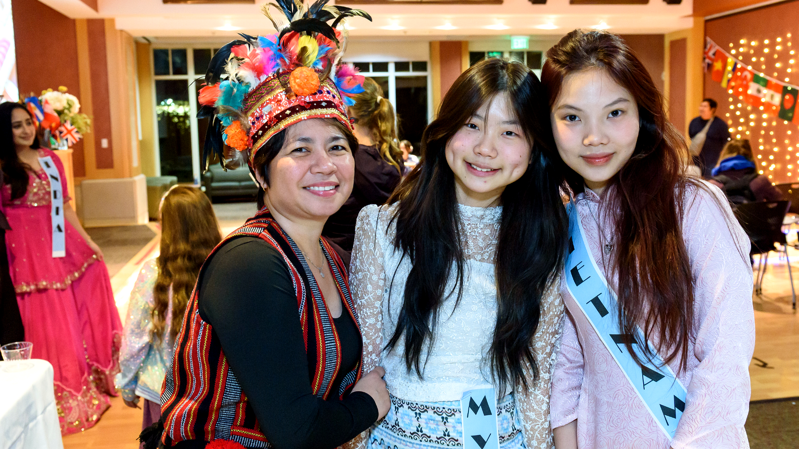 Three students in cultural attire posing together at an international event.