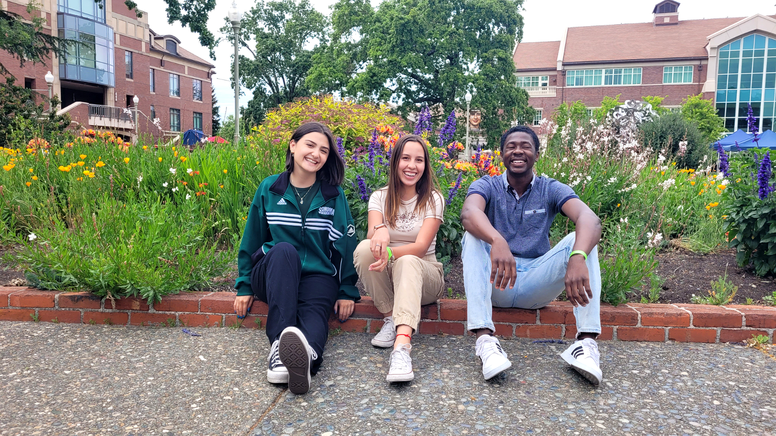 Three students sitting together in front of a colorful flower garden on the SRJC campus.